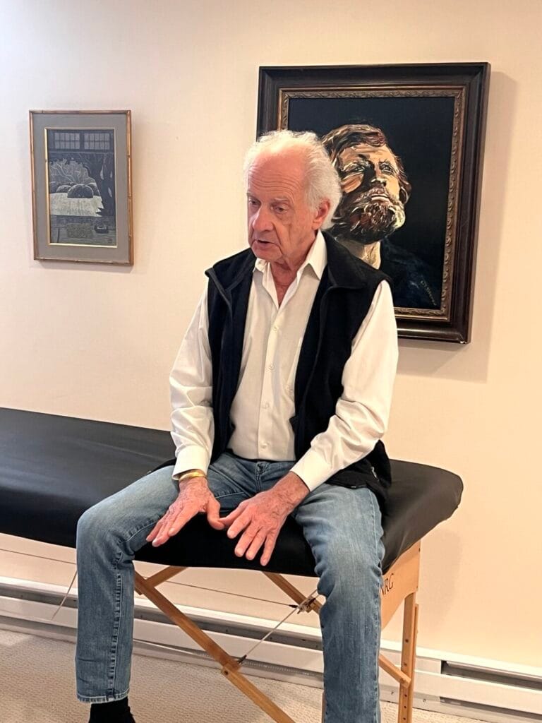 Tommy Thompson seated at a table, guiding students through a focused Alexander Technique session with attentive presence.