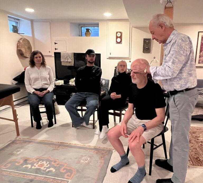 Tommy Thompson demonstrating kinesthetic awareness and triadic resonance through hands-on Alexander Technique instruction with trainees seated in a group setting.