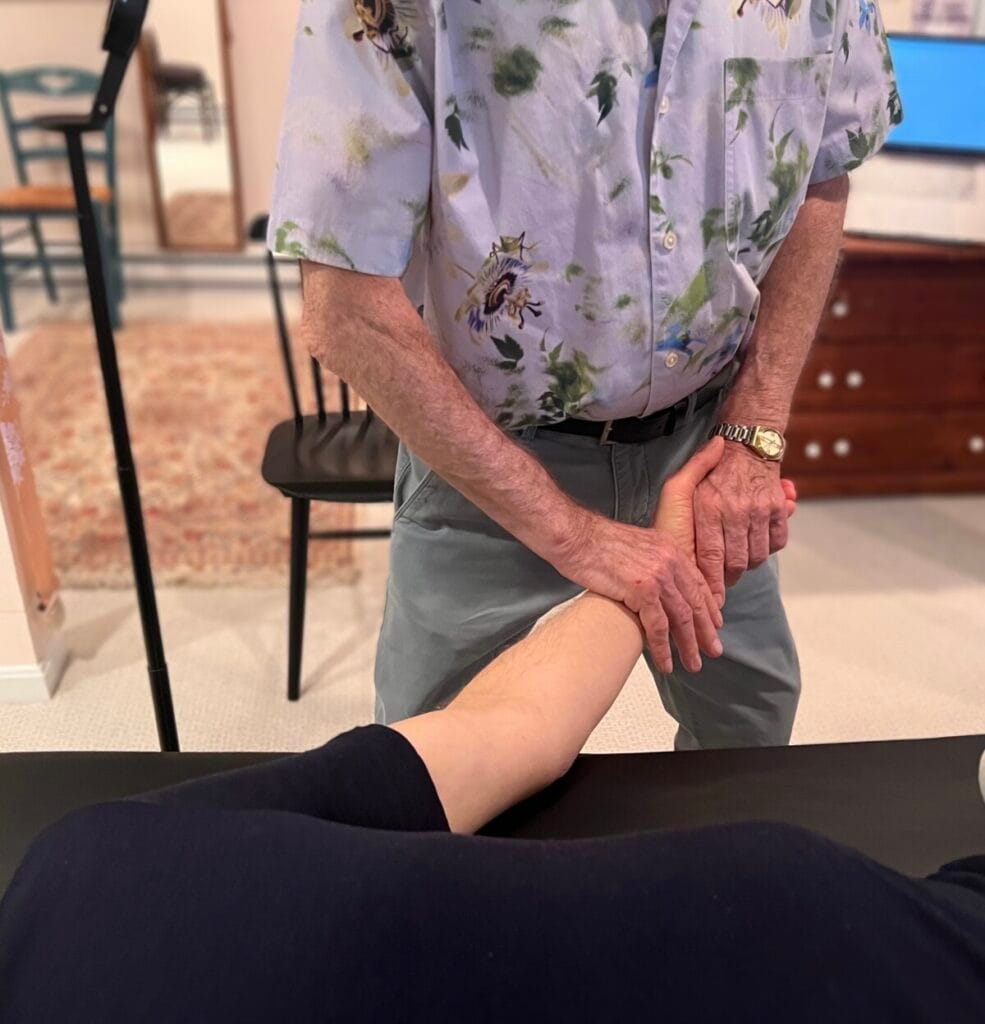 Alexander Technique teacher Tommy Thompson gently using touch to support a participant’s wrist and guide sensory awareness