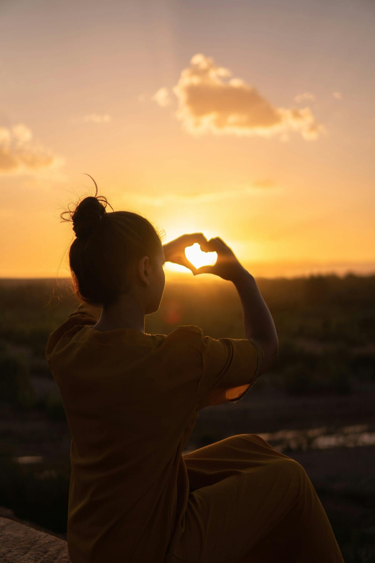 A woman forms a heart shape with her hands at sunset, expressing presence and self-awareness—key themes in embodied identity and the Alexander Technique.
