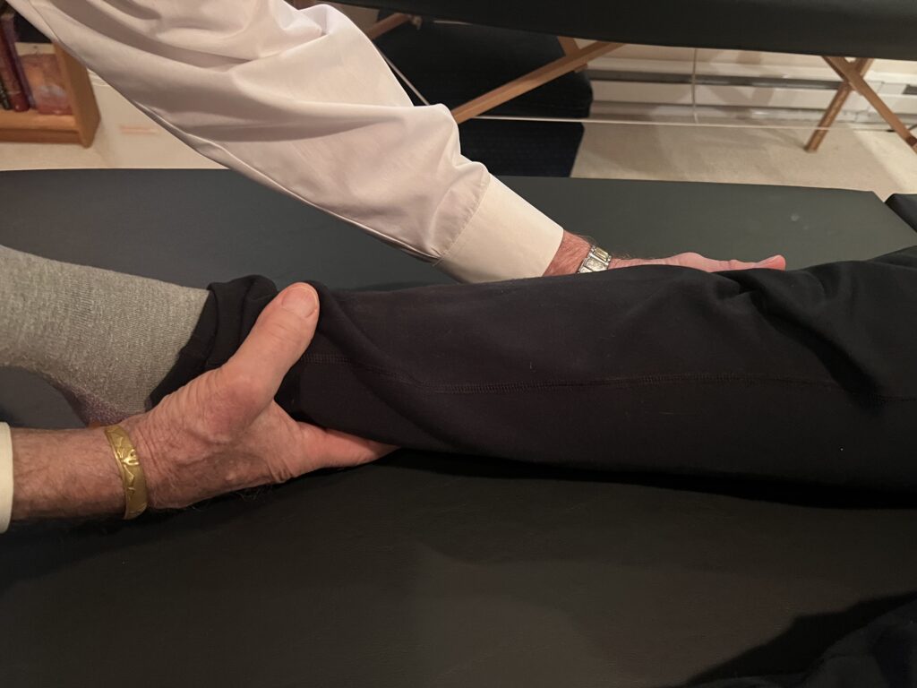 Teacher supporting student’s lower legs with both hands during hands-on technique in Class 12