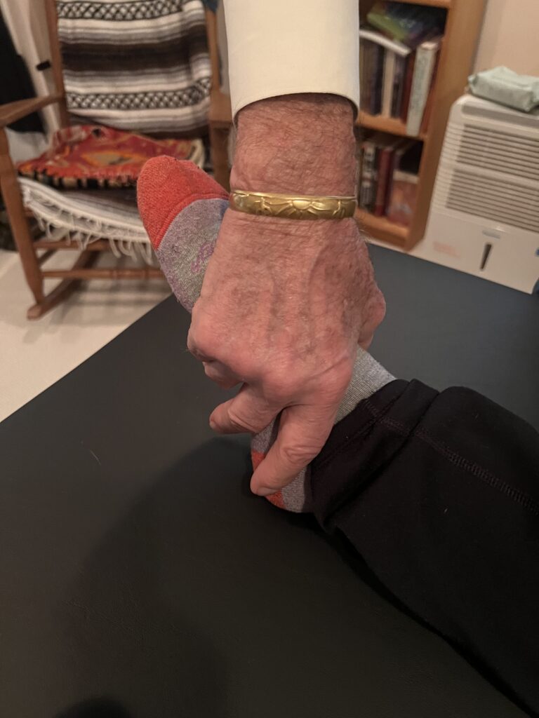 Close-up of teacher’s hands gently contacting student’s feet in an Alexander Technique hands-on session (Class 12)