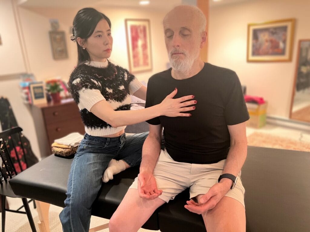 Ari applying gentle hands-on guidance to a fellow trainee's chest during an Alexander Technique class, focusing on breath, awareness, and nervous system alignment.
