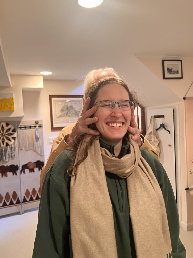 A trainee smiling with closed eyes while Tommy Thompson gently places his hands on her head during an Alexander Technique class on nervous system alignment.