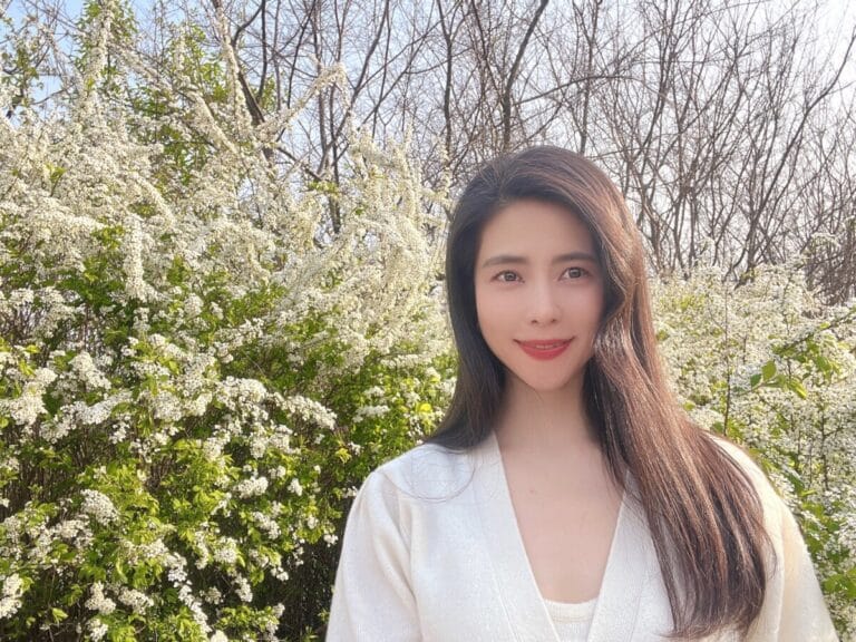 Ari Kim standing calmly in front of white blossoms, representing her journey of self-restoration through the Alexander Technique.