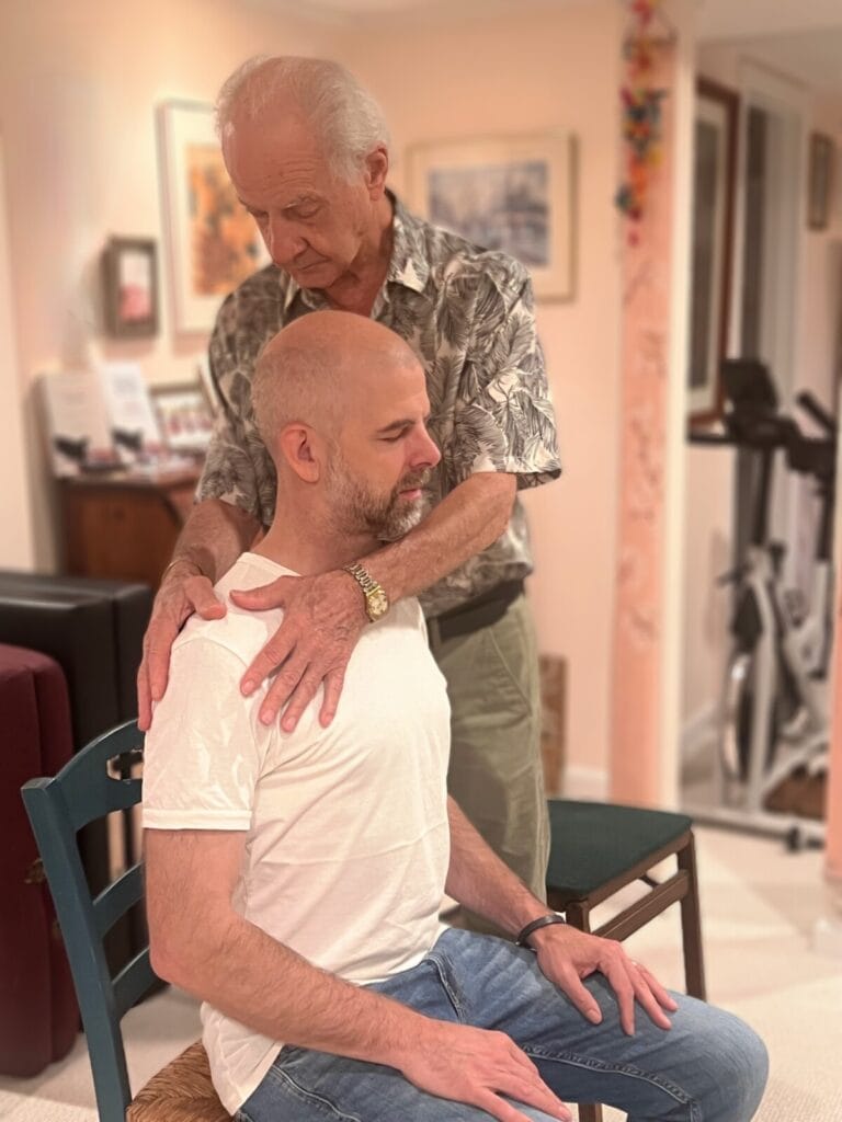 Tommy Thompson guiding a trainee through Alexander Technique hands-on work during Class 77, demonstrating withholding definition and listening touch.